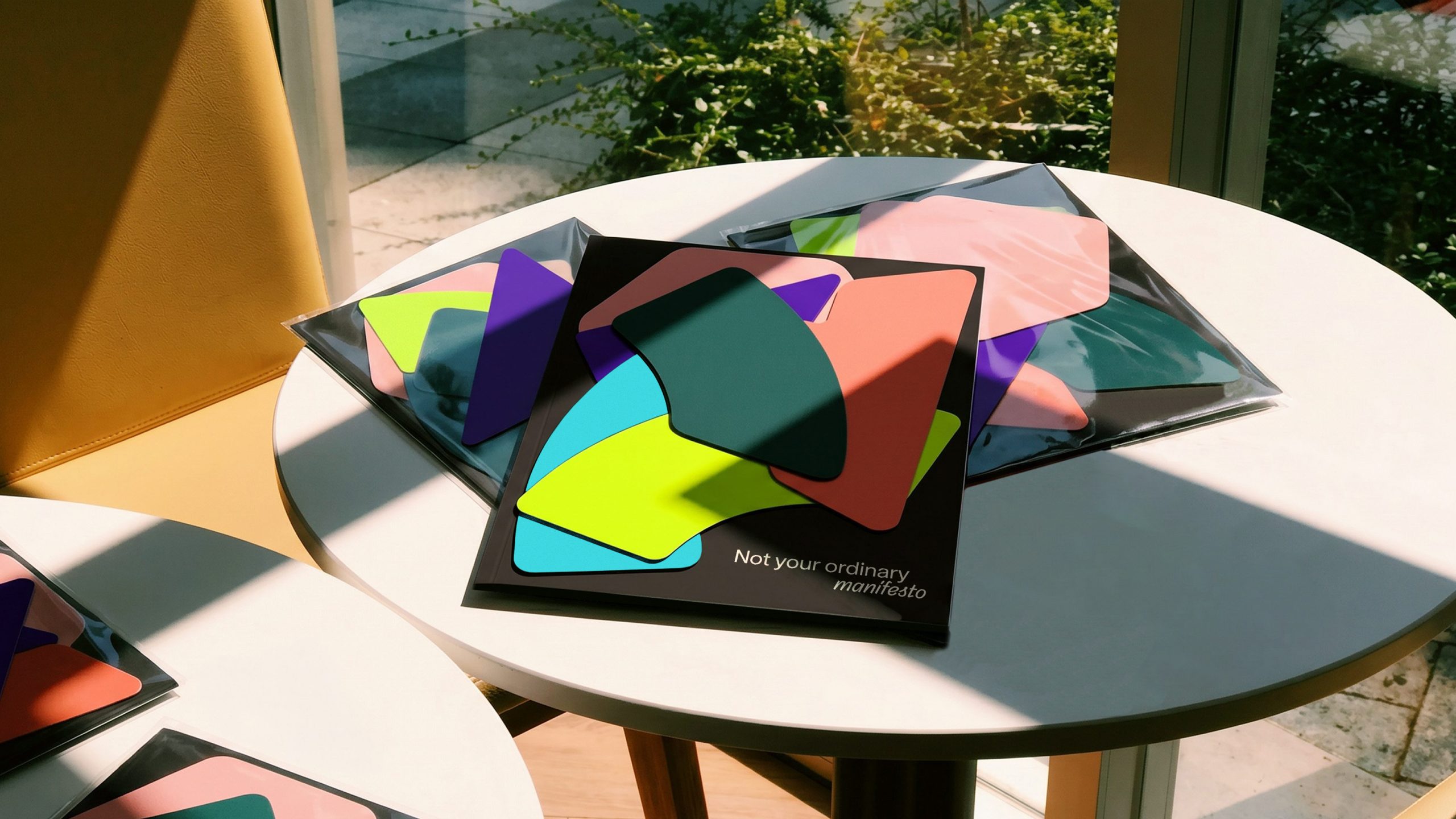 Folder reading "Not your ordinary manifesto" surrounded by colourful geometric branding on an outdoor table