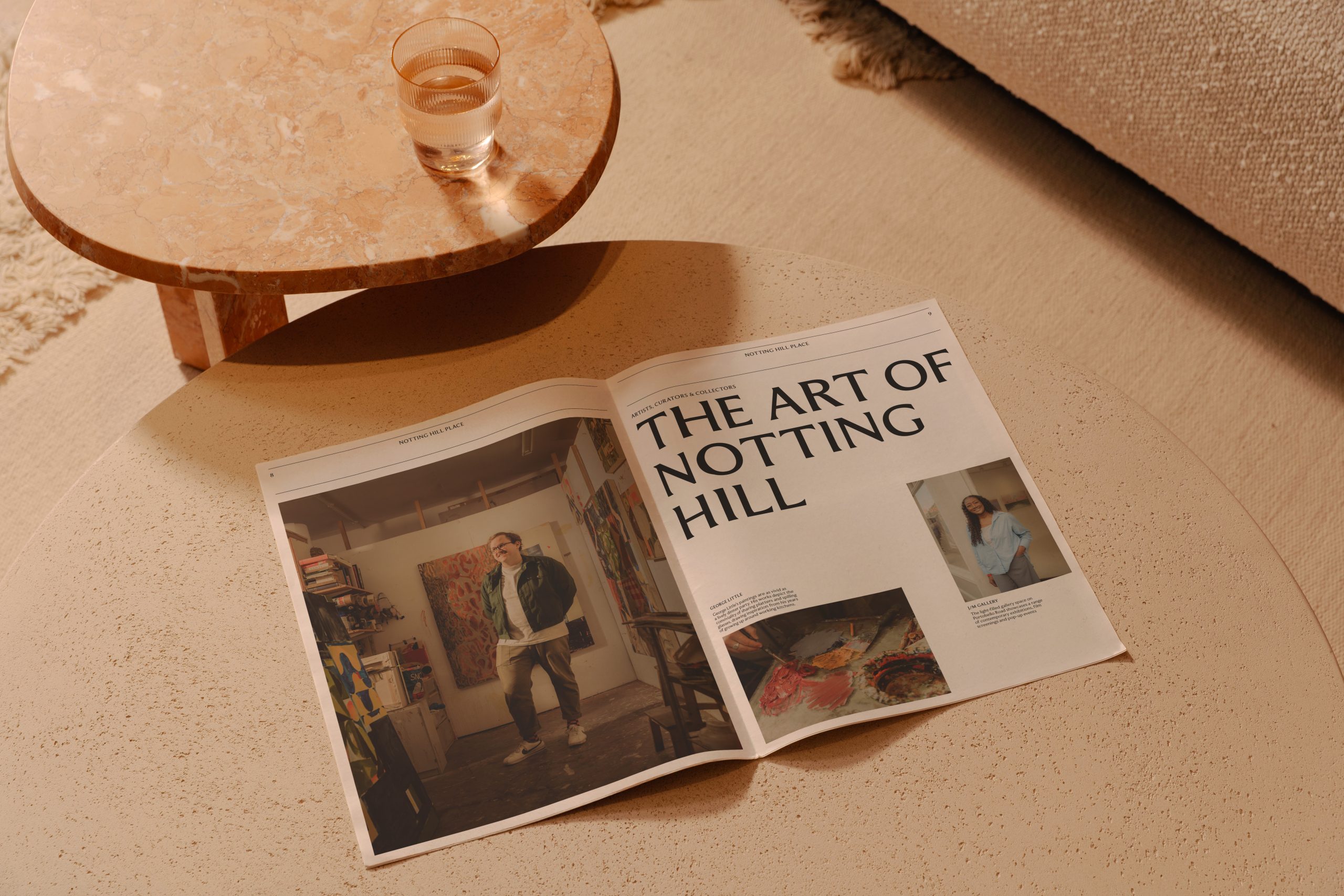 Open magazine spread titled 'The Art of Notting Hill' on a floor beside a marble side table with a glass of water