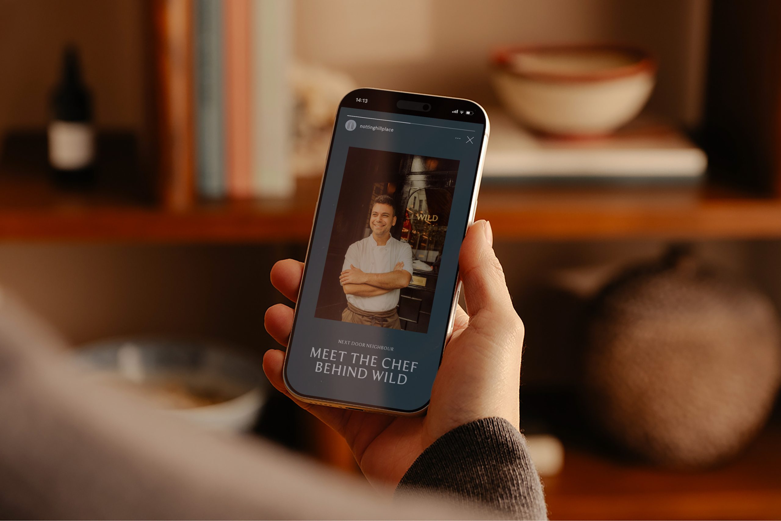 Hand holding a phone showing a Notting Hill Place Instagram story titled 'Meet the Chef Behind Wild' with a chef portrait