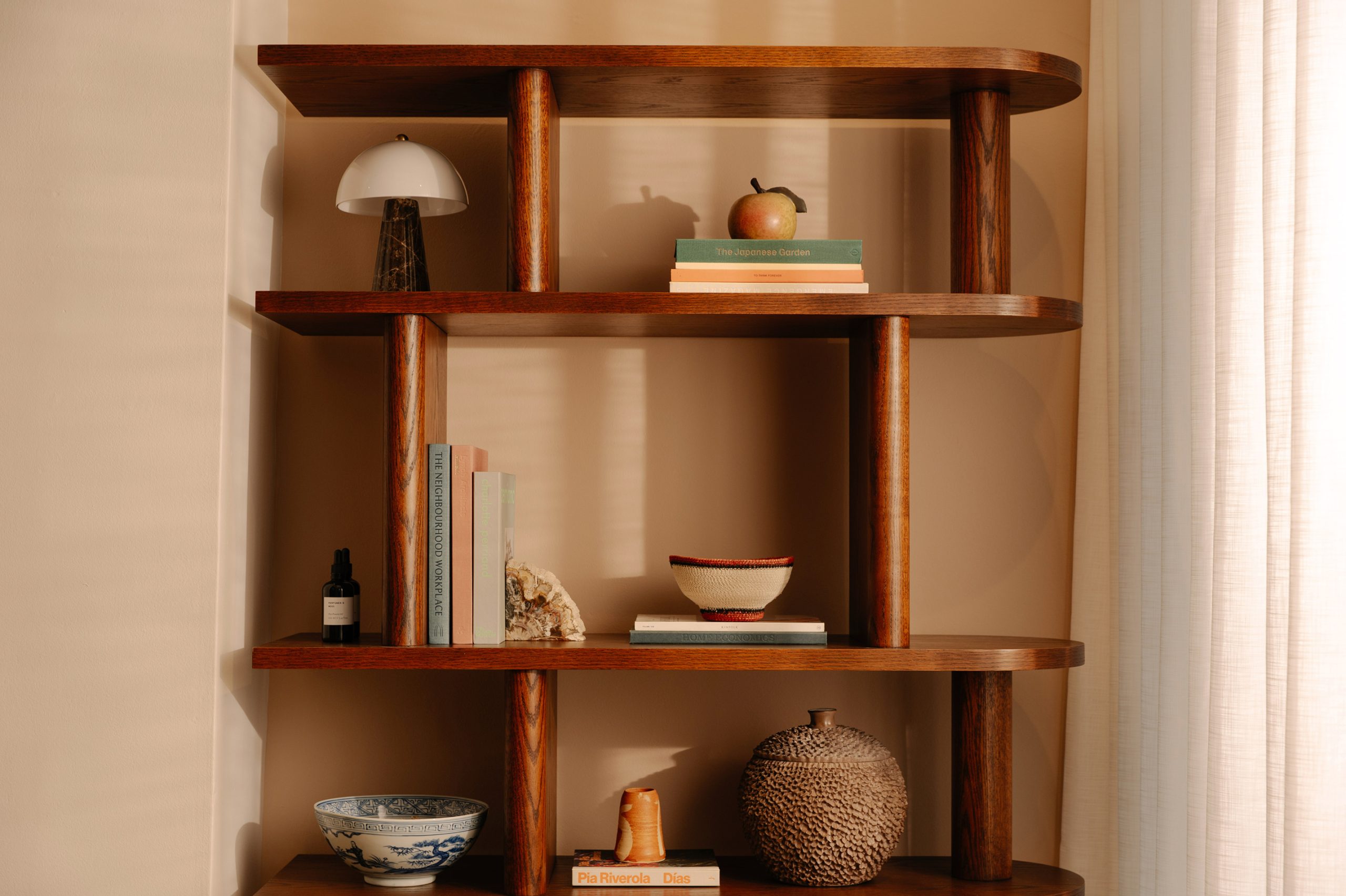 Wooden shelving unit styled with books, ceramic bowls, a mushroom lamp, and decorative objects in a warmly lit room